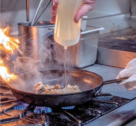 Chef cooking fresh ingredients in a cast iron pan over an open flame at a Rusted Rake Brewing restaurant kitchen