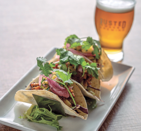 Soft tacos filled with slow-cooked meat, pickled onions, and fresh herbs, served with craft beer at Rusted rake brewing